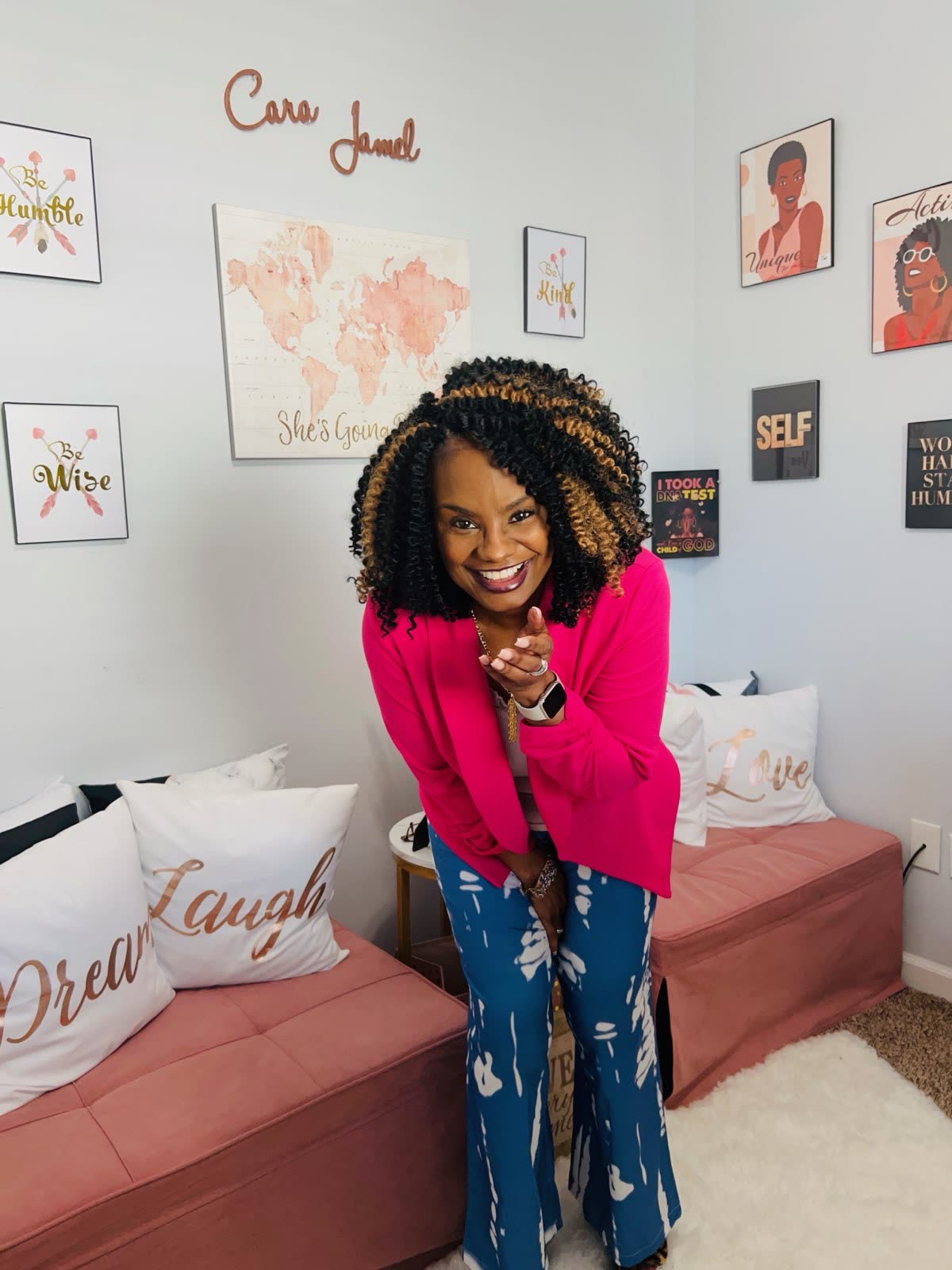 Cara smiling in her office under a wall sign reading Cara Jamel